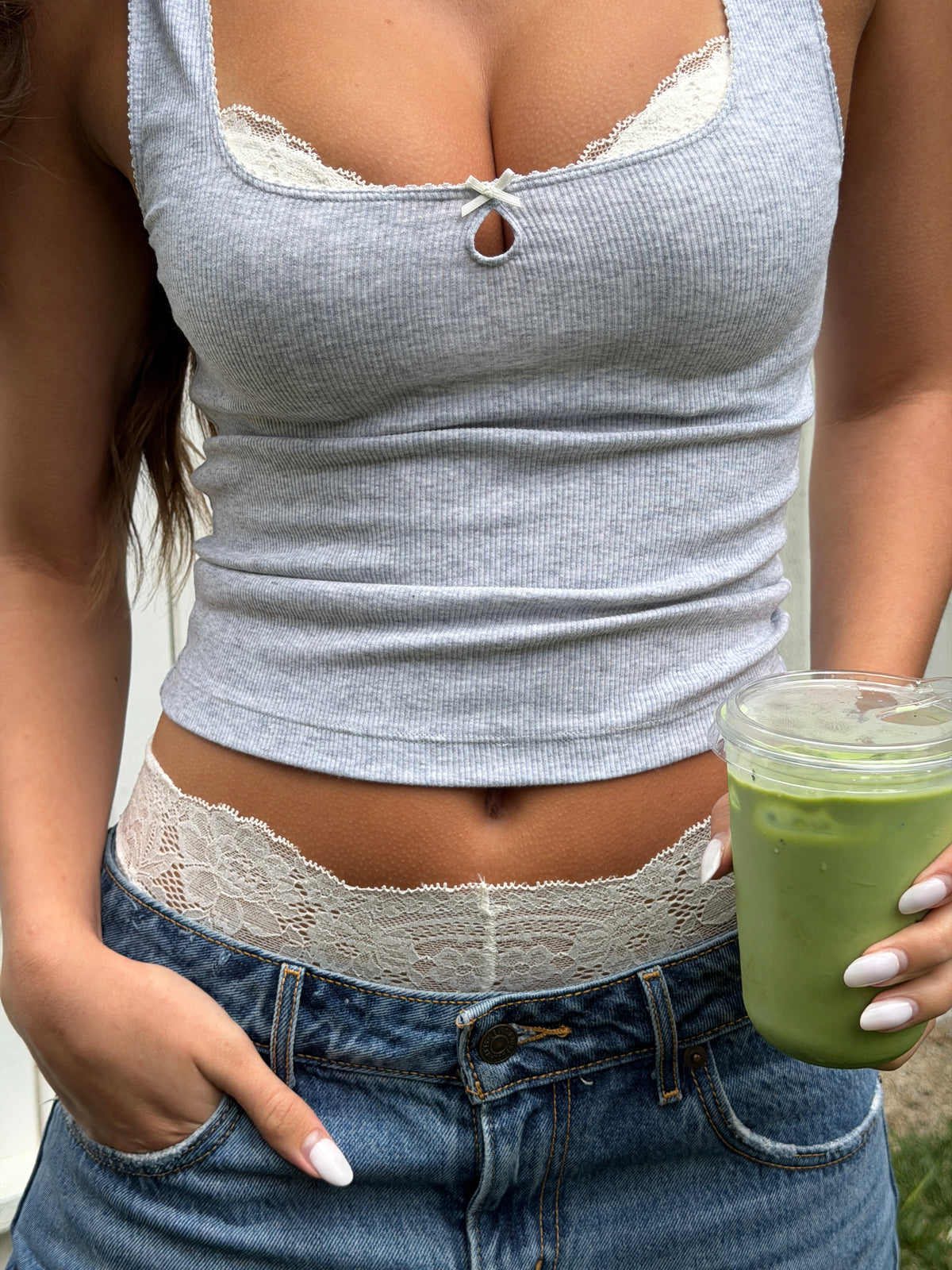 Person wearing a gray tank top with lace details and blue jeans, holding a matcha.