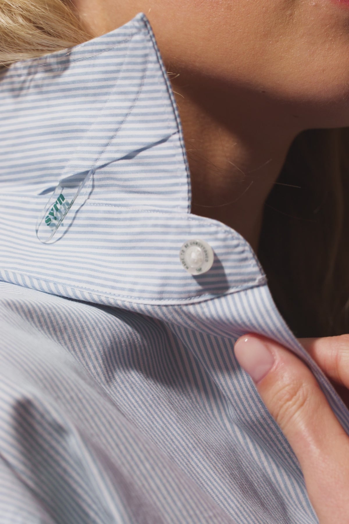 Freya showing the hidden details of a collar stay and engraved buttons on a blue and white striped button down shirt